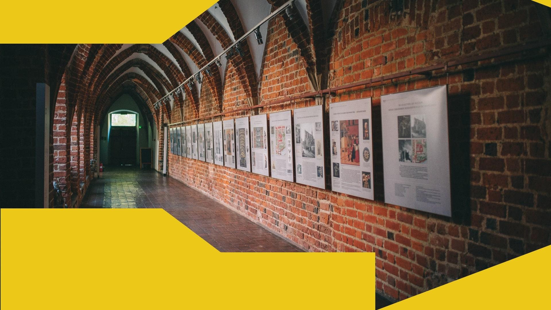 Zdjęcie wnętrza Muzeum Architektury we Wrocławiu z wyeksponowanymi na ścianach pracami