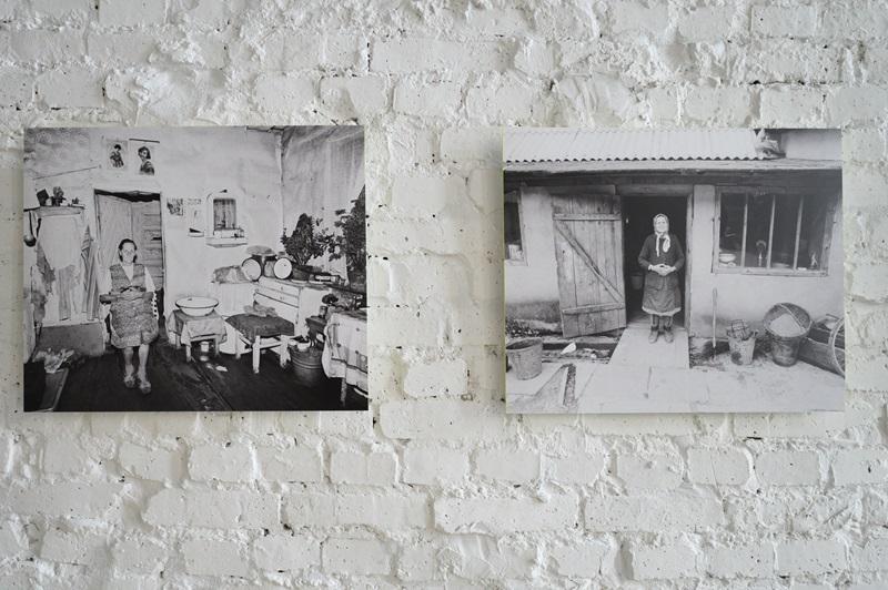 Dwie fotografie autorstwa Zofii Rydet wyeksponowane na ścianie. Na pierwszej widać kobietę stojącą w kuchni, gdzie widać sprzęty kuchenne i wystrój typowy dla lat 70.  Na drugim zdjęciu widać kobietę stojącą w progu domu. Na podwórku widać metalowe i drewniane kubły oraz grabie.