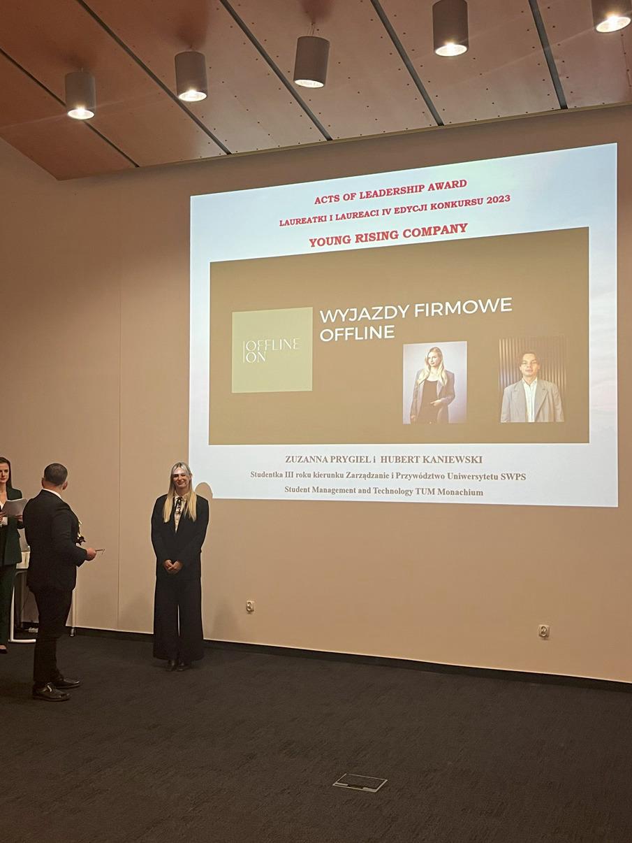 Dwie studentki rozmawiające z prowadzącą warsztaty, wszystkie trzymają w rękach elementy wycięte z kartonu i sklejki. 
