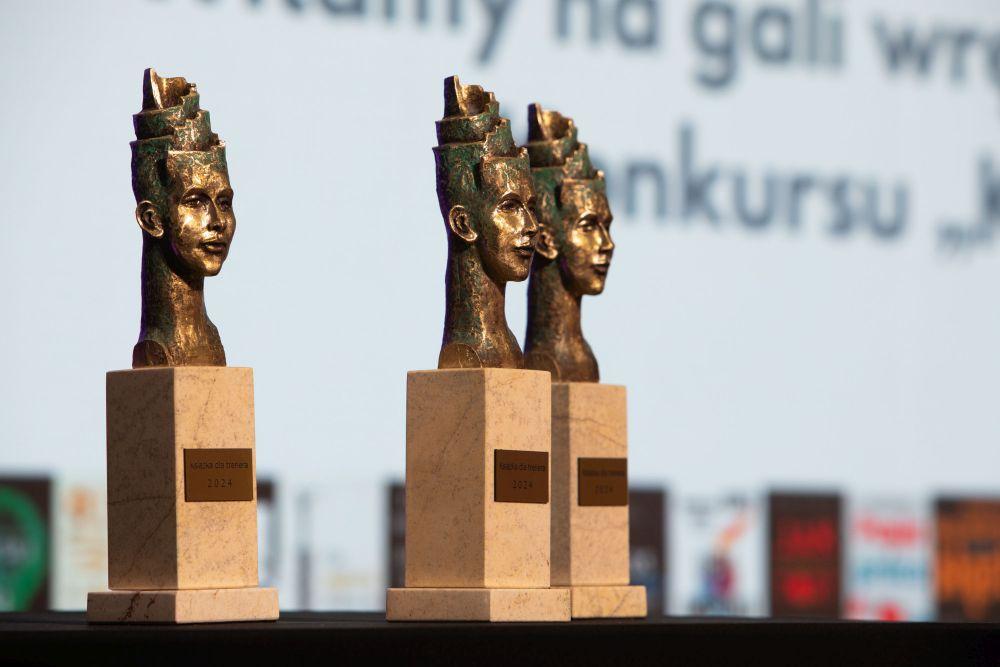 Trzy złote statuetki w kształcie twarzy z napisem „Książka dla trenera 2024”