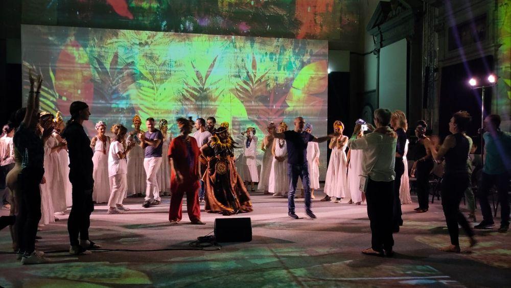 Duża grupa osób na scenie, w tym aktorki w strojach. Fotograf robi zdjęcia