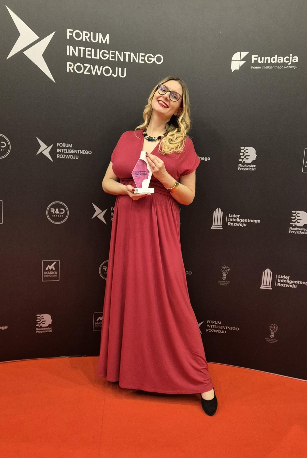 Dr Wróblewska stojąca ze statuetką na czerwonym dywanie, w tle widać ściankę z napisem Forum Inteligentnego Rozwoju
